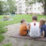 3 Jungs sitzen zusammen auf dem Spielplatz vor den Mietwohnungen