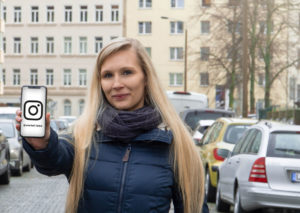 Junge Frau steht auf einer Straße und hält Smartphone in die Kamera