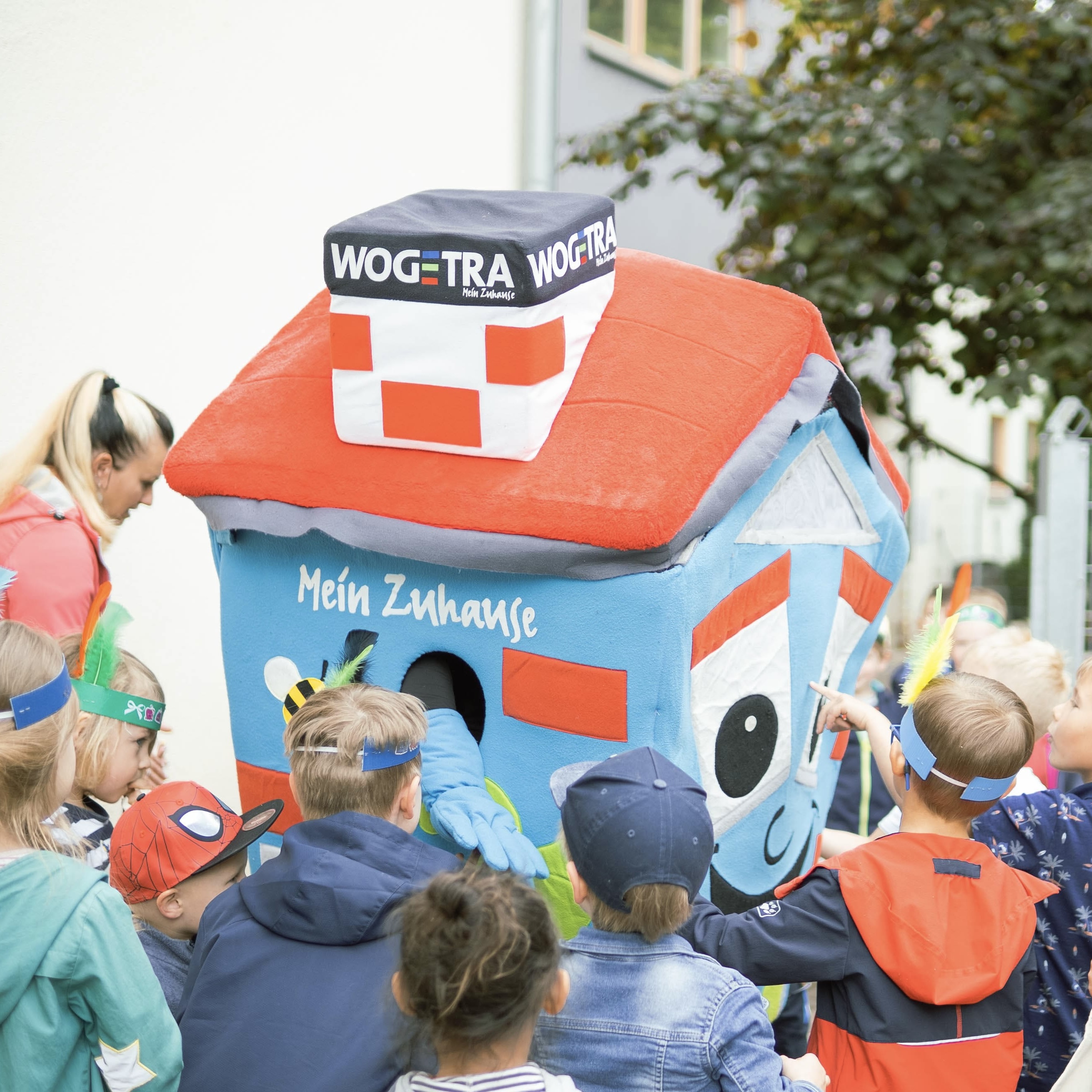 Ein Maskottchen in Form eines Hauses verteilt Geschenke an Kindergartenkinder.