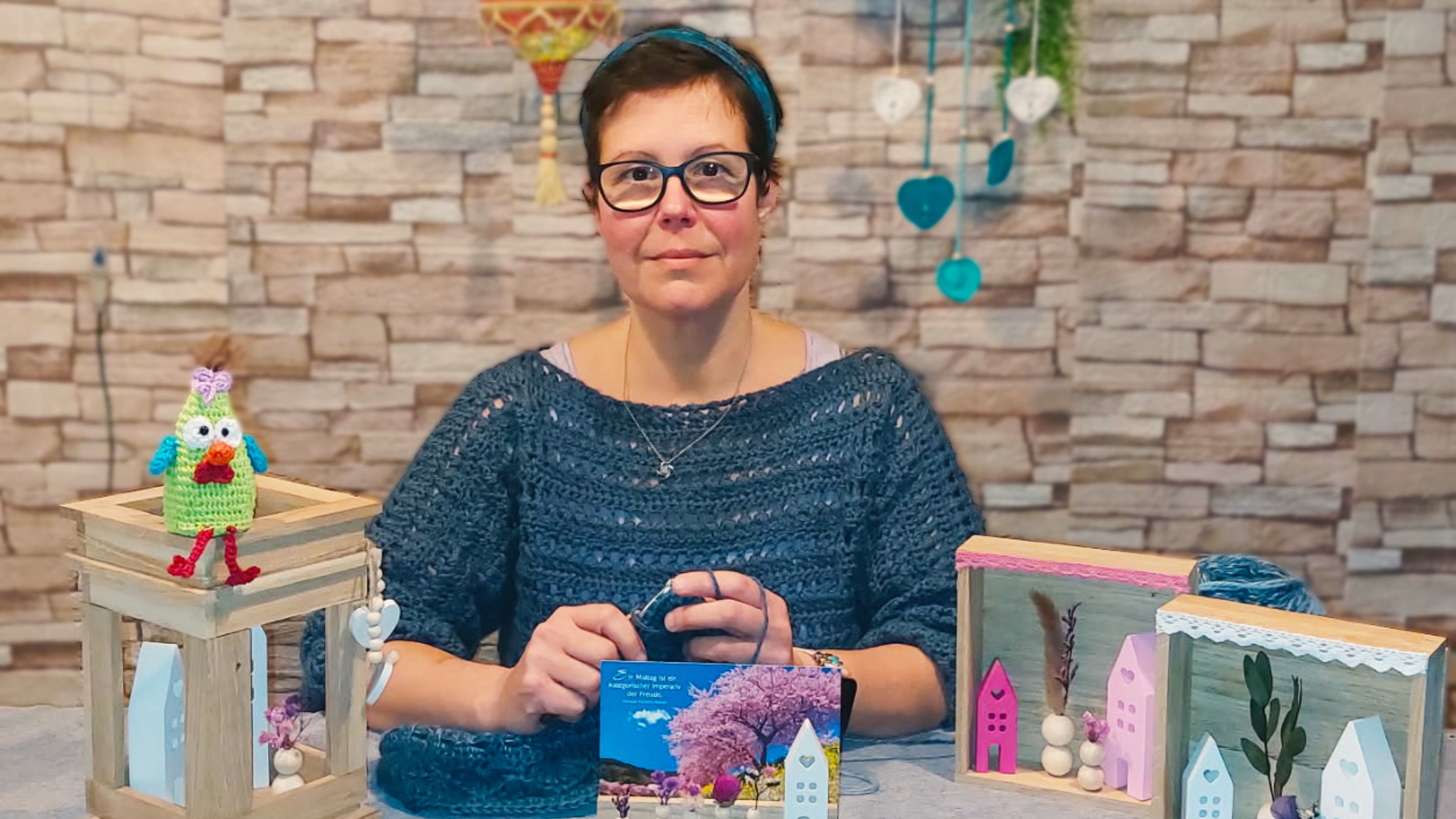 Das Logo von „Kreativ in Thekla“ zeigt ein Wollknäuel in Herzform mit Häkelnadel, eingerahmt von einem floralen Rundbogen, mit dem Slogan „Mit Liebe für dich“.